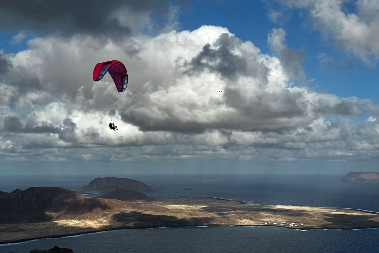 A paraglider above the northern cliffs of Lanzarote, with La Graciosa and the islets beyond