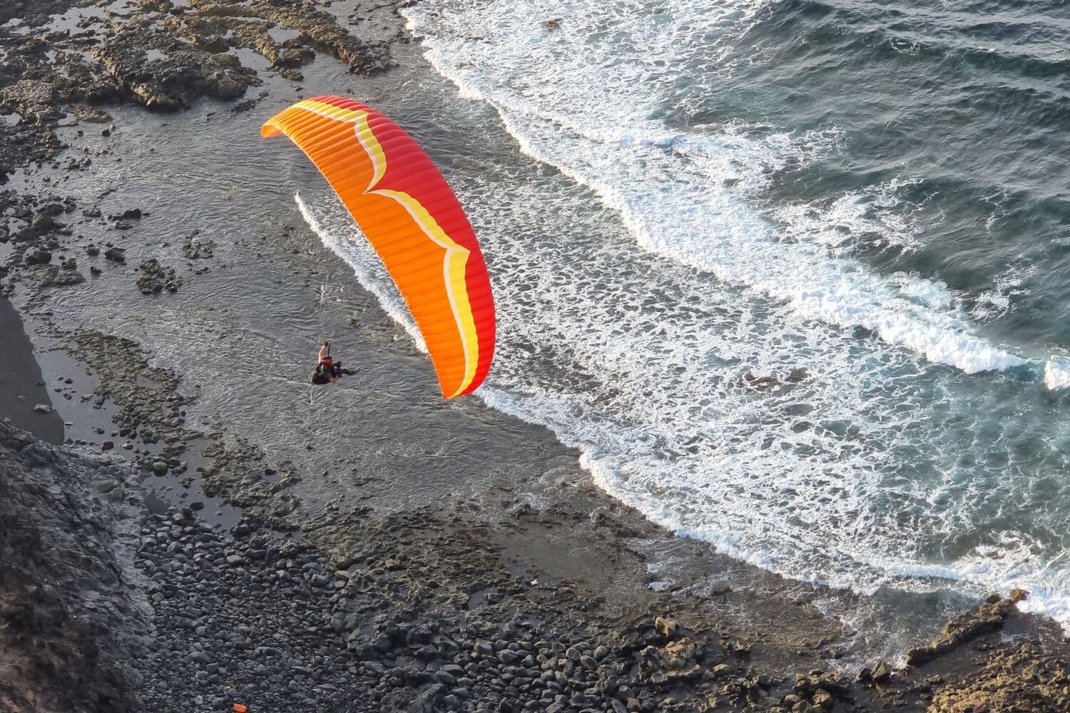A paraglider soaring over the surf and black rock at Tenesar, in the north-west of Lanzarote