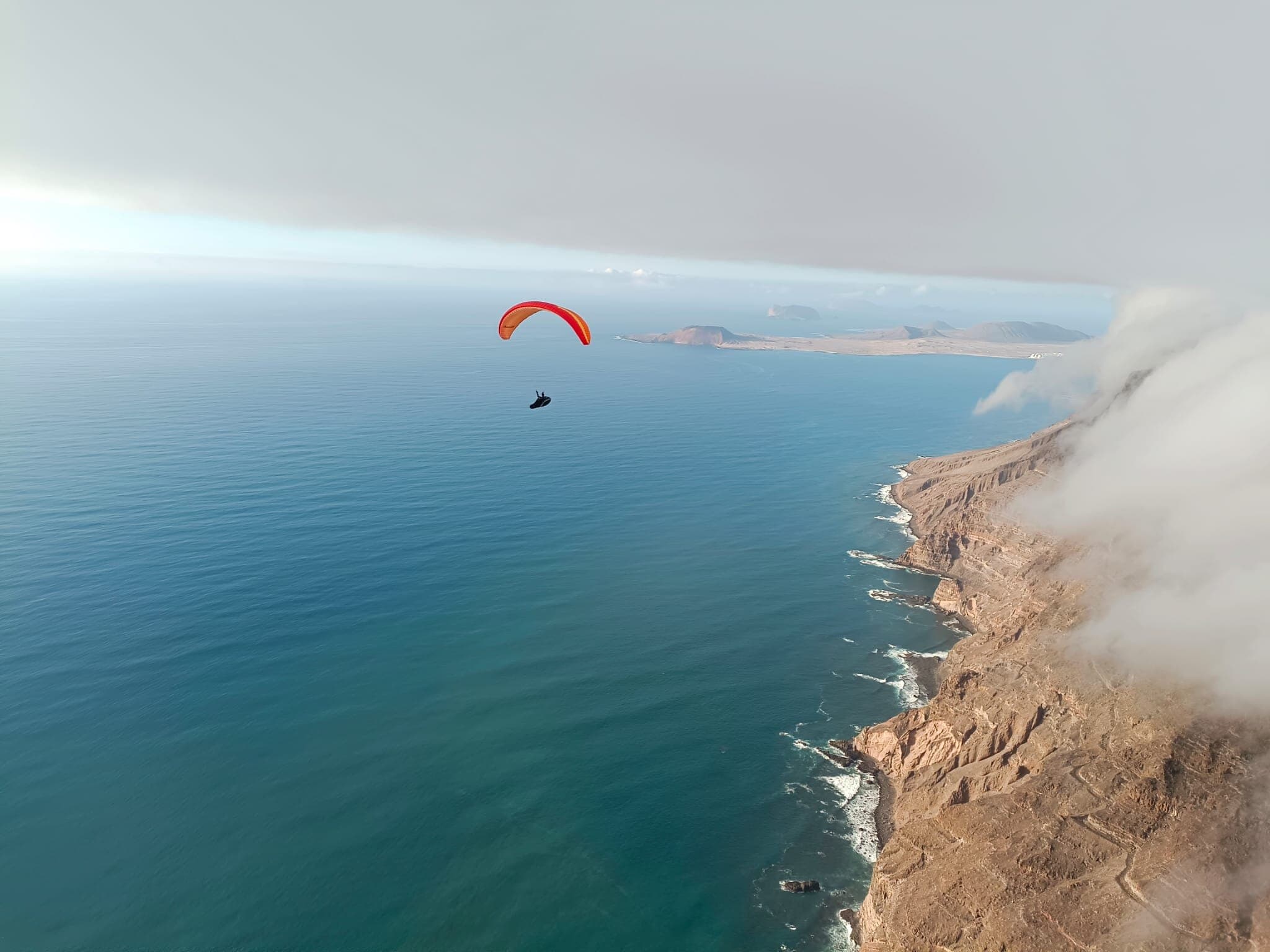 Paragliding in Lanzarote: a paraglider soaring the Famara cliffs, with La Graciosa in the distance