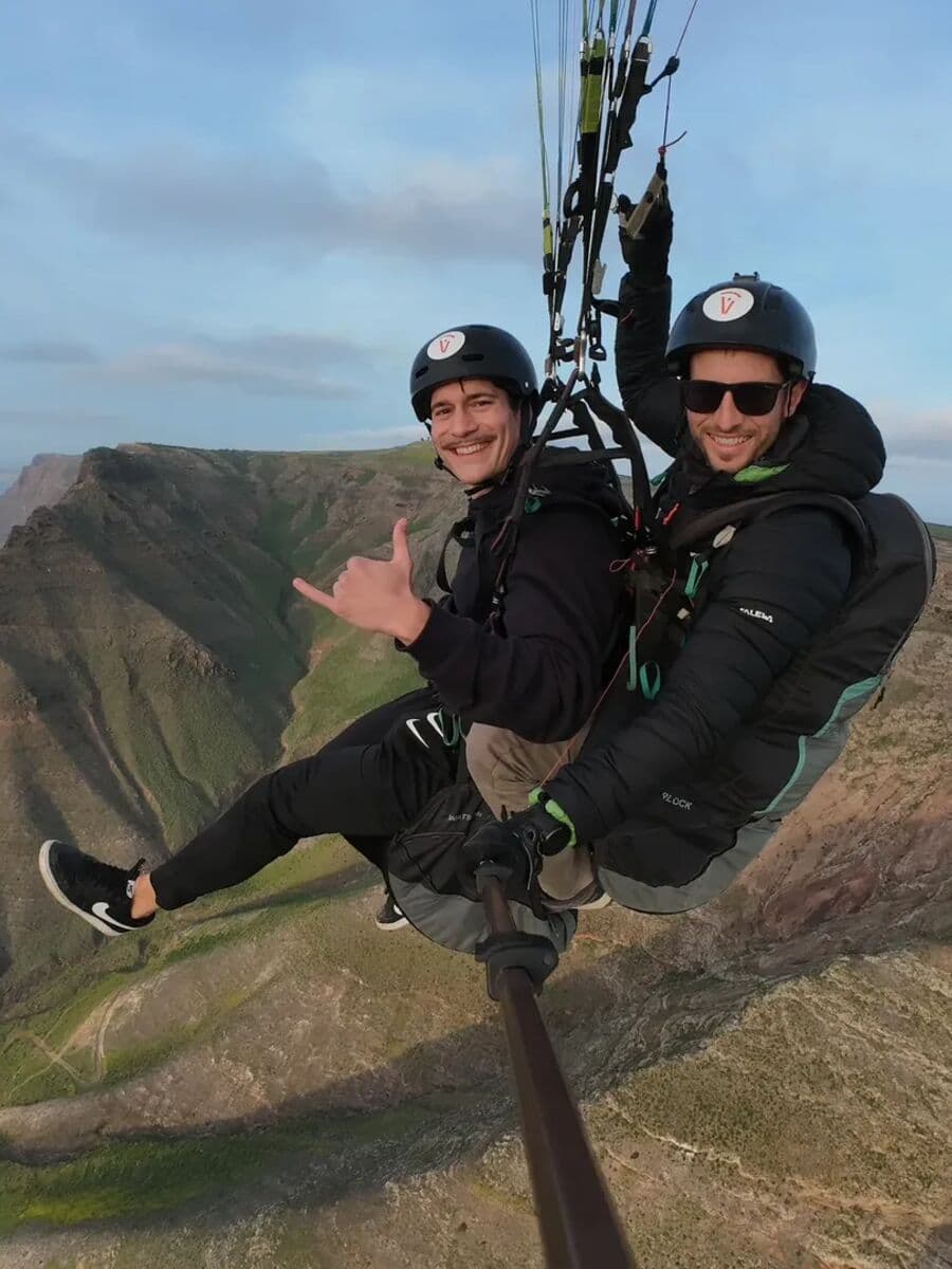 Piloto y pasajero de biplaza haciendo el saludo shaka sobre el risco de Famara